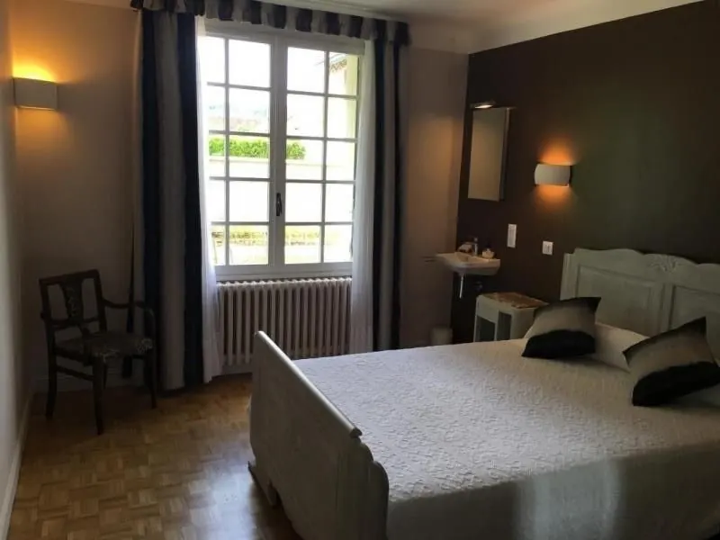 Chambre double aux murs chocolat avec lit en bois peint, lavabo et fenêtre sur le jardin