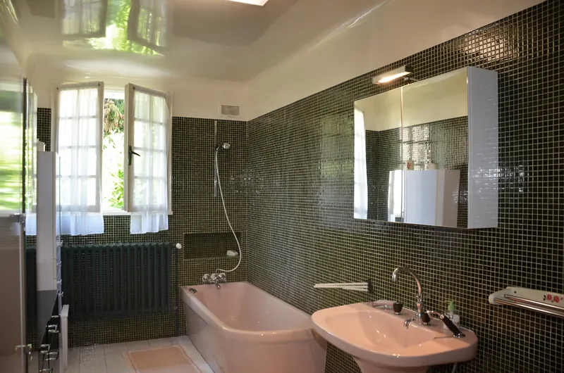 Salle de bain du gîte carrelée de mosaïque sombre, avec baignoire et double vasque